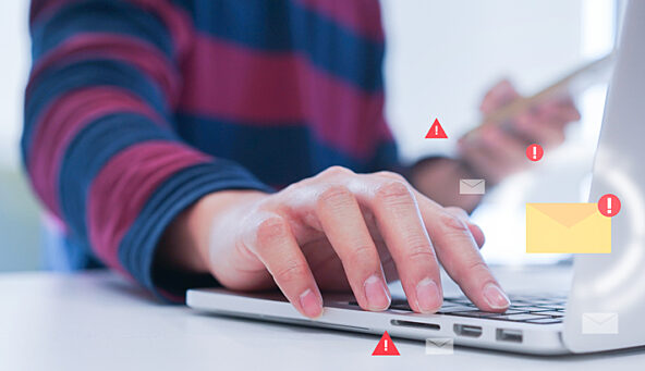 A photo of someone’s hand on a laptop keyboard with illustrated email icons and warning symbols popping up around the computer.